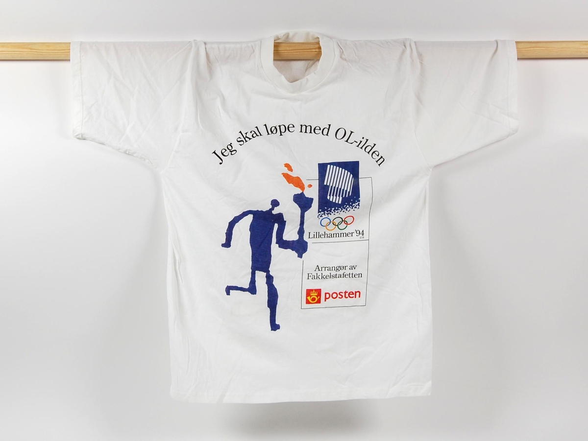 Hvit t-skjorte med flerfarget logo for de olympiske vinterleker på Lillehammer i 1994 og Posten. Blått og oransje piktogram av fakkelmannen utgjør motivet på t-skjorten.