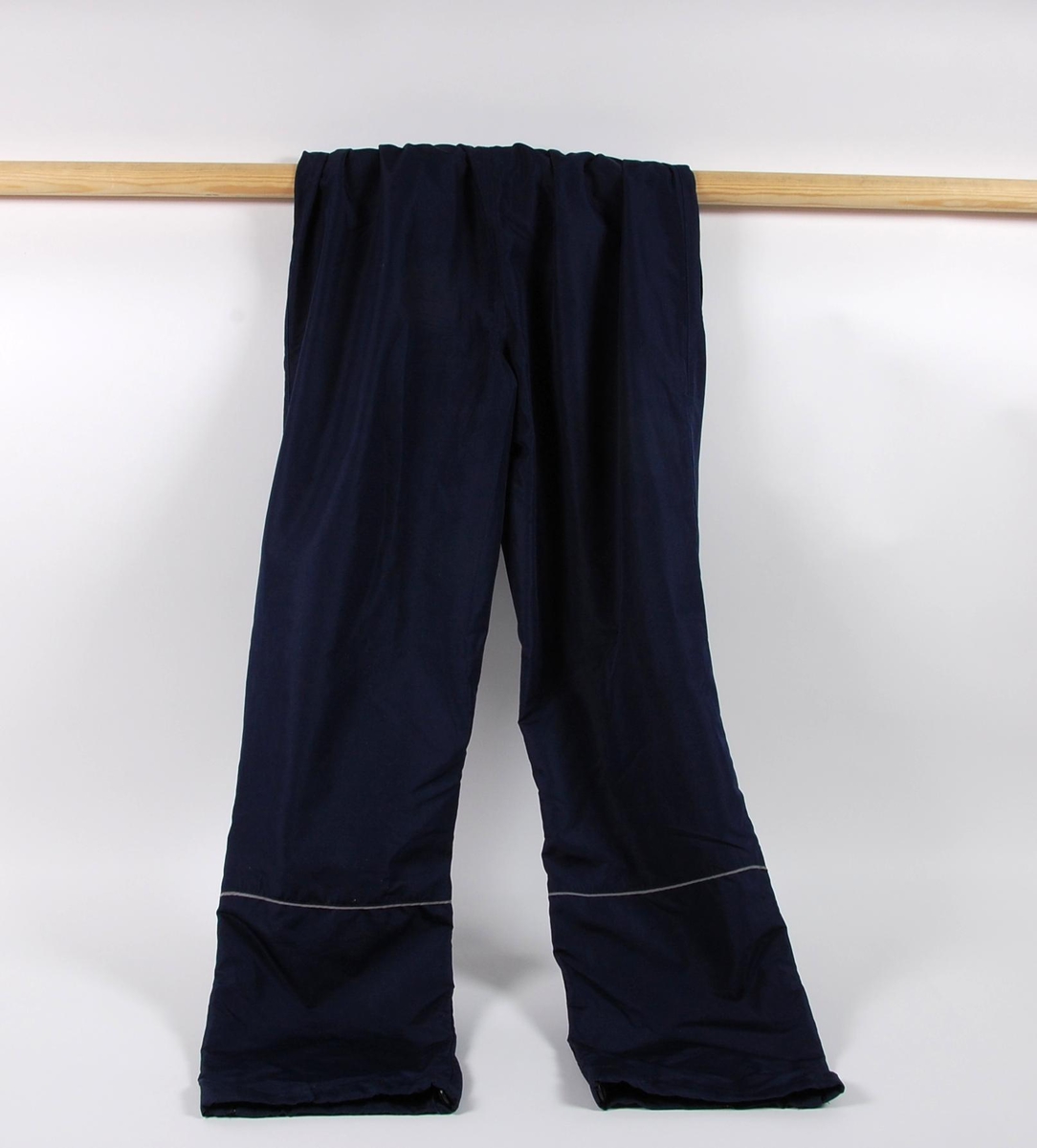 Blå overtrekksbukse med logo for UMBRO. Buksen har glidelås nederst ved hver ben, og refleksstriper på venstre ben. Buksestørrelsen er S.