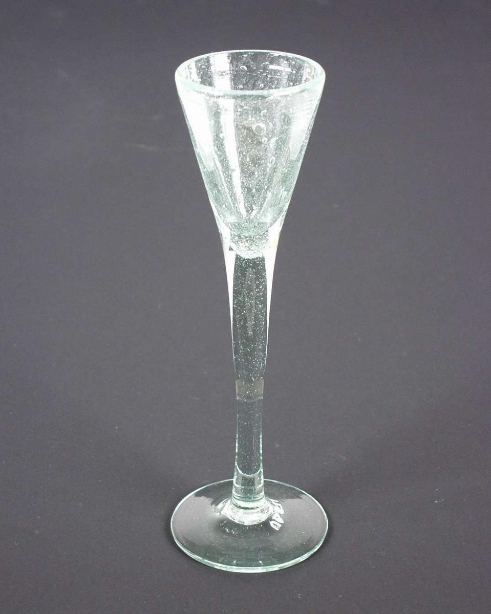 Brennevinsglass, spissglass, med høy stett. Glasset er svakt grønt.