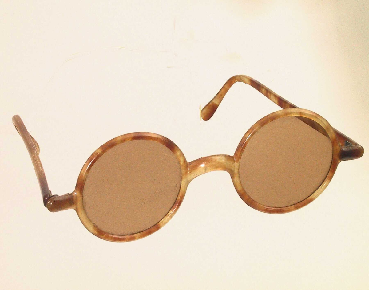 Solbriller  Lysbrunt   
glass.  Skillpaddefarget celluloid. Sirkelrunde glass i "hornbrilleinnfatning", lysbrun og gyllengul.