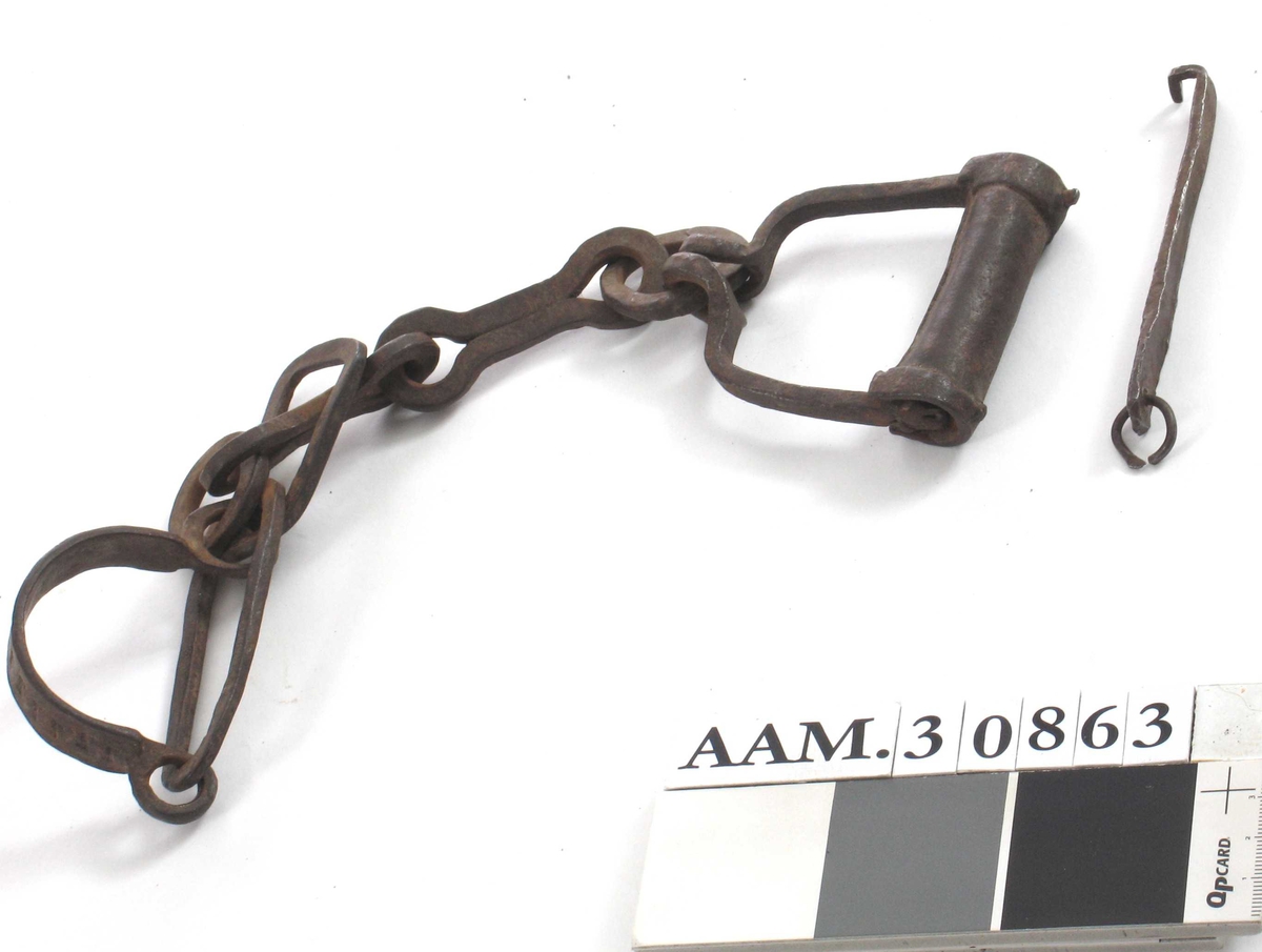 Slavelenke med lås og nøkkel, for barn. To bøyler av jern, forbundet med lenke, nøkkelhull i den ene bøylen.

Deler:  a = lenken   b = nøkkel