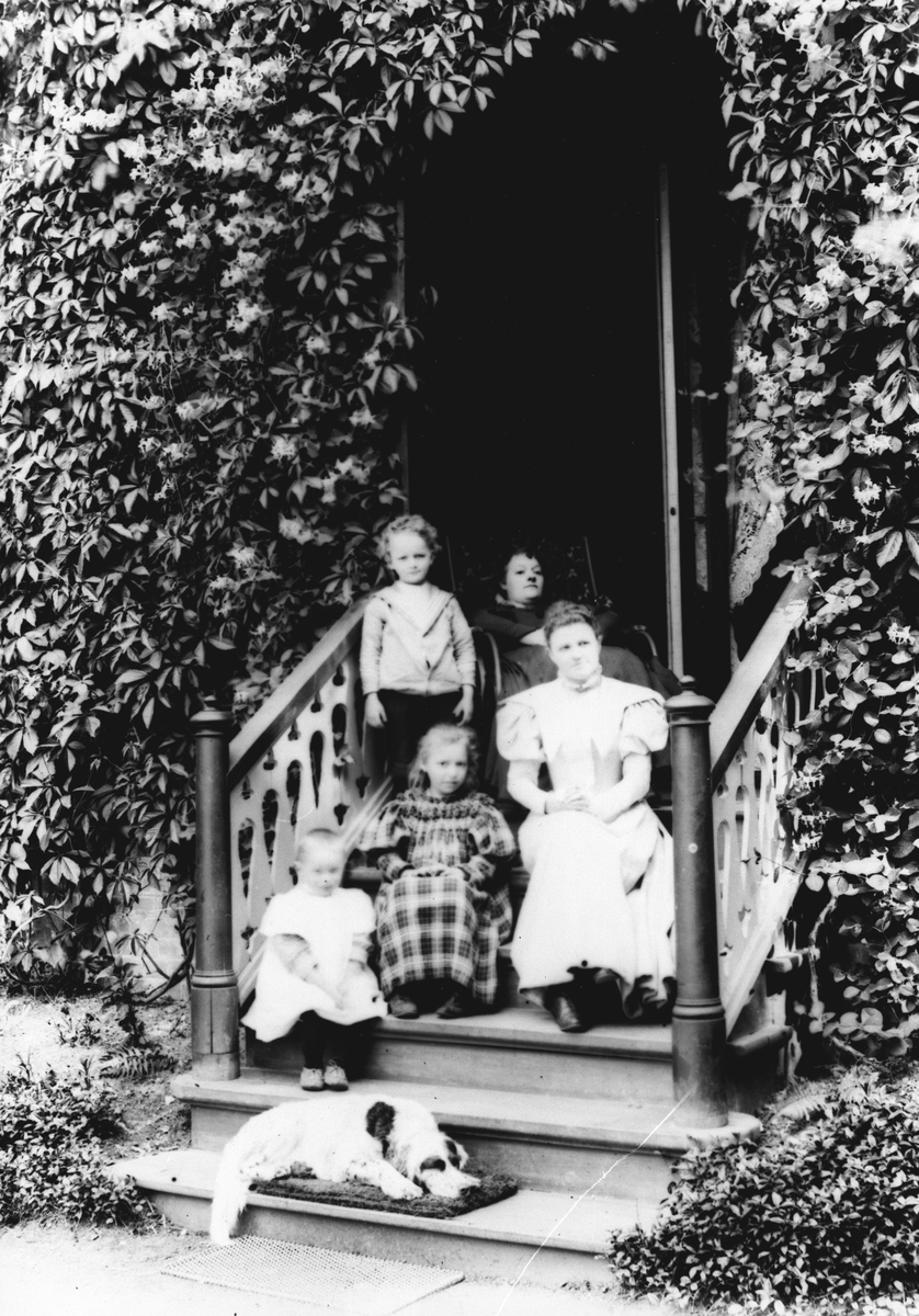 To damer og tre barn sittende på trappa ute.