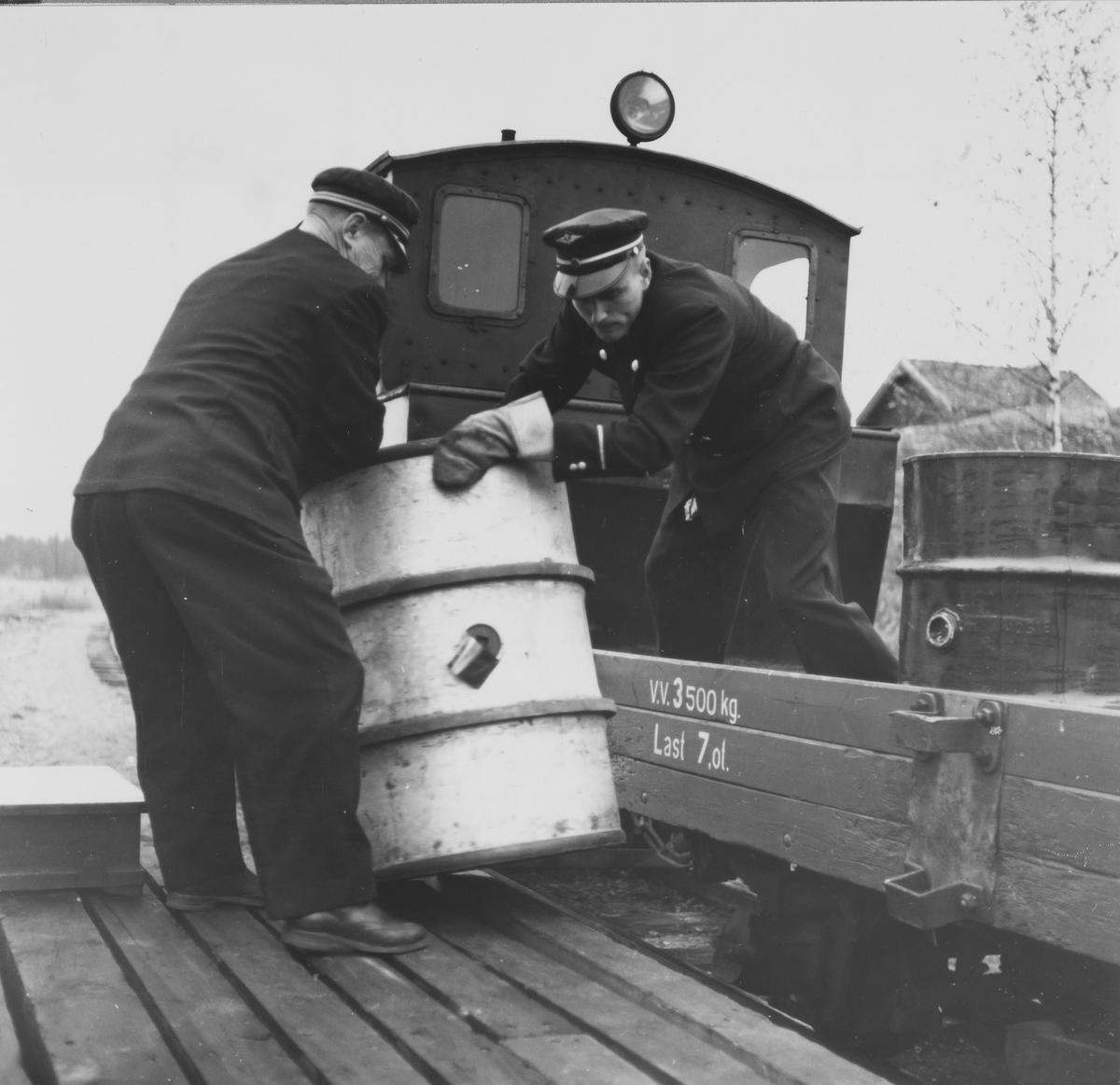 Overkonduktør Rolf Ødegård og konduktør Sigmund Furustad losser et oljefat fra en N-vogn. Tog retning Skulerud
