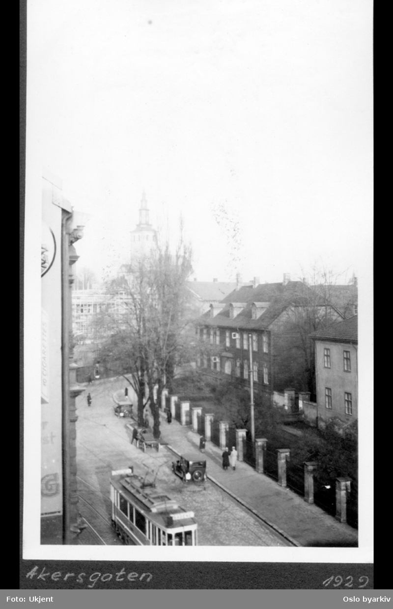 Akersgata ved Militærhospitalet og del av Empirekvartalet. Gatemiljø med bl.a. trikk. Forhager med hekker og busker.Tårnet på Margaretakyrkan i bakgrunnen.