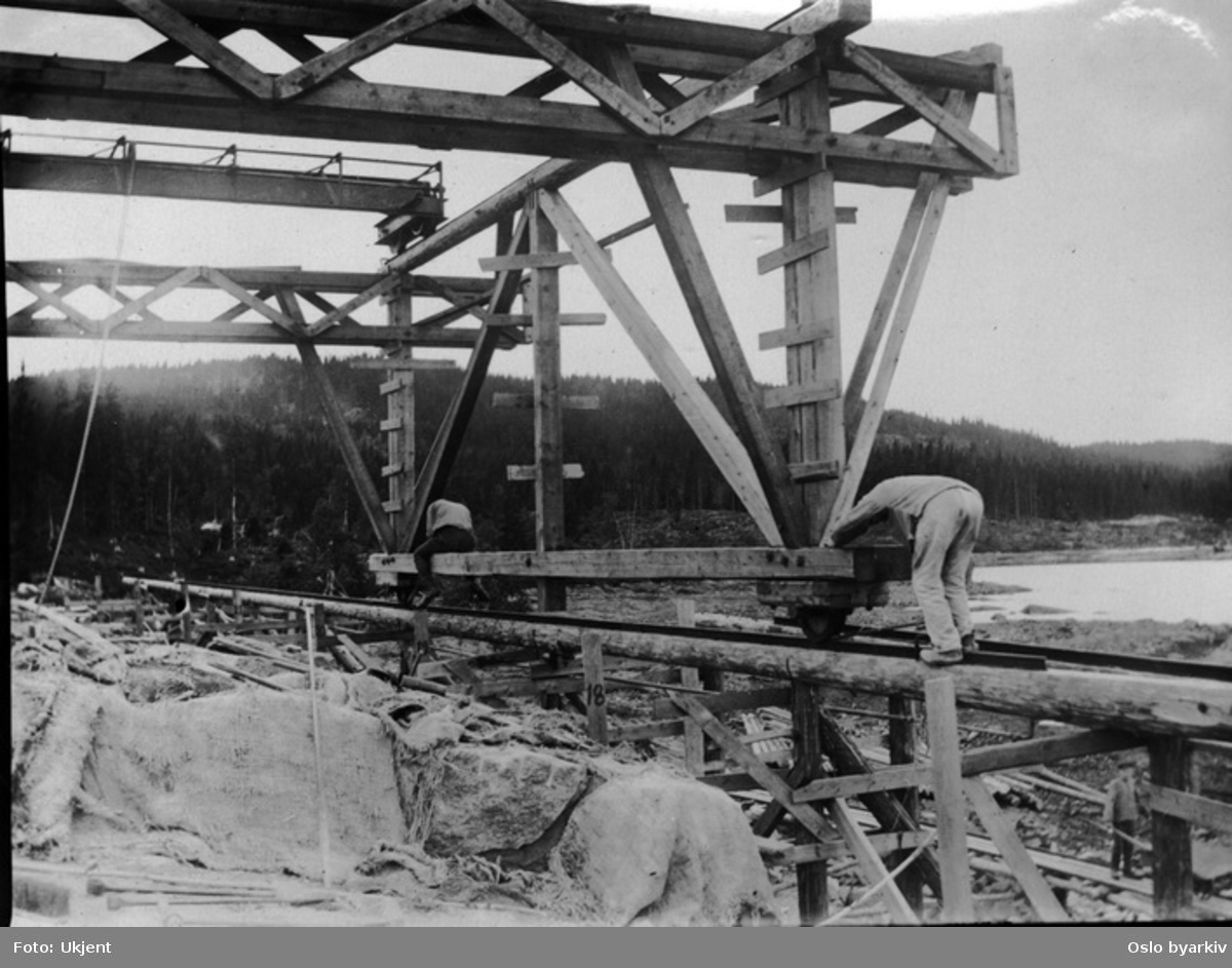 Fra byggingen av dammen (ferdig 1911). Reisverk i tre / Arbeidsplattform langs steindammen. Løfteinnretning for steinblokker.