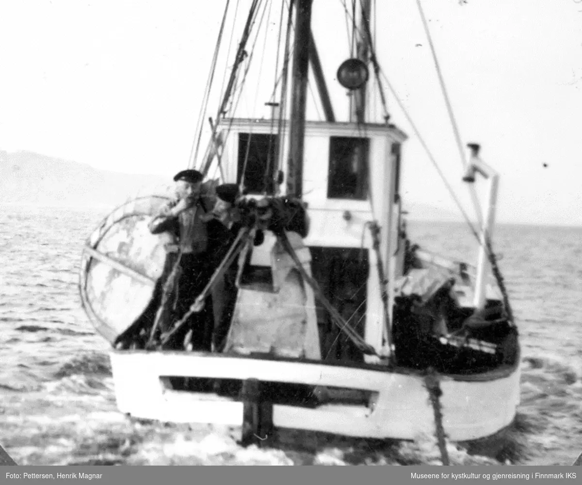 Evakuering 1944. Jentoft Andersen ombord i båten sin "Blex" på vei til Tromsø To mindre båter henger på slep og Jentoft tar en titt for å sjekke om alt er i orden.