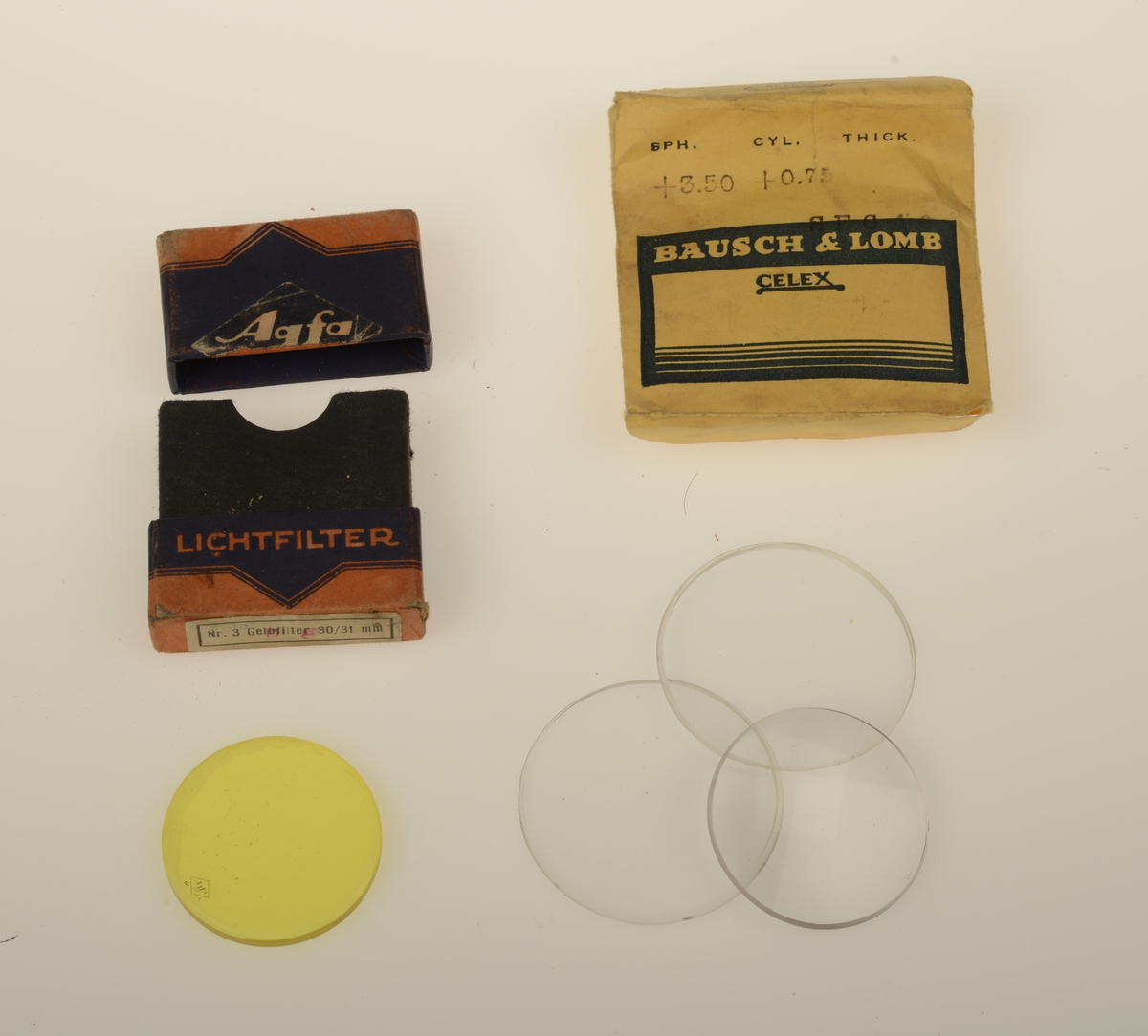 3 brilleglass. 2 er like, og et mindre er konvekst i pose merker Bausch & Lomb. Gulfilter i egen eske merket Agfa.