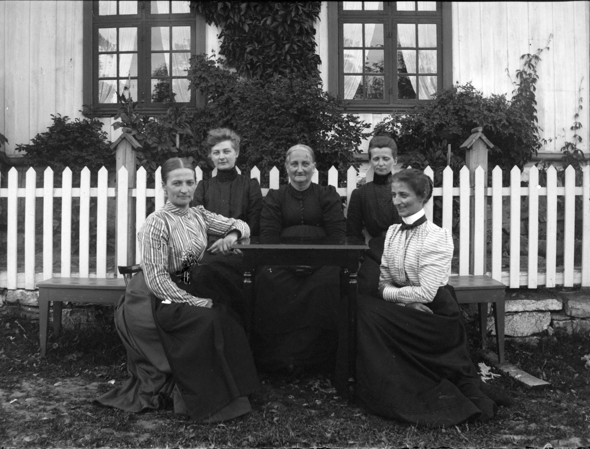 Fem kvinner foran et hus med gjerde. 