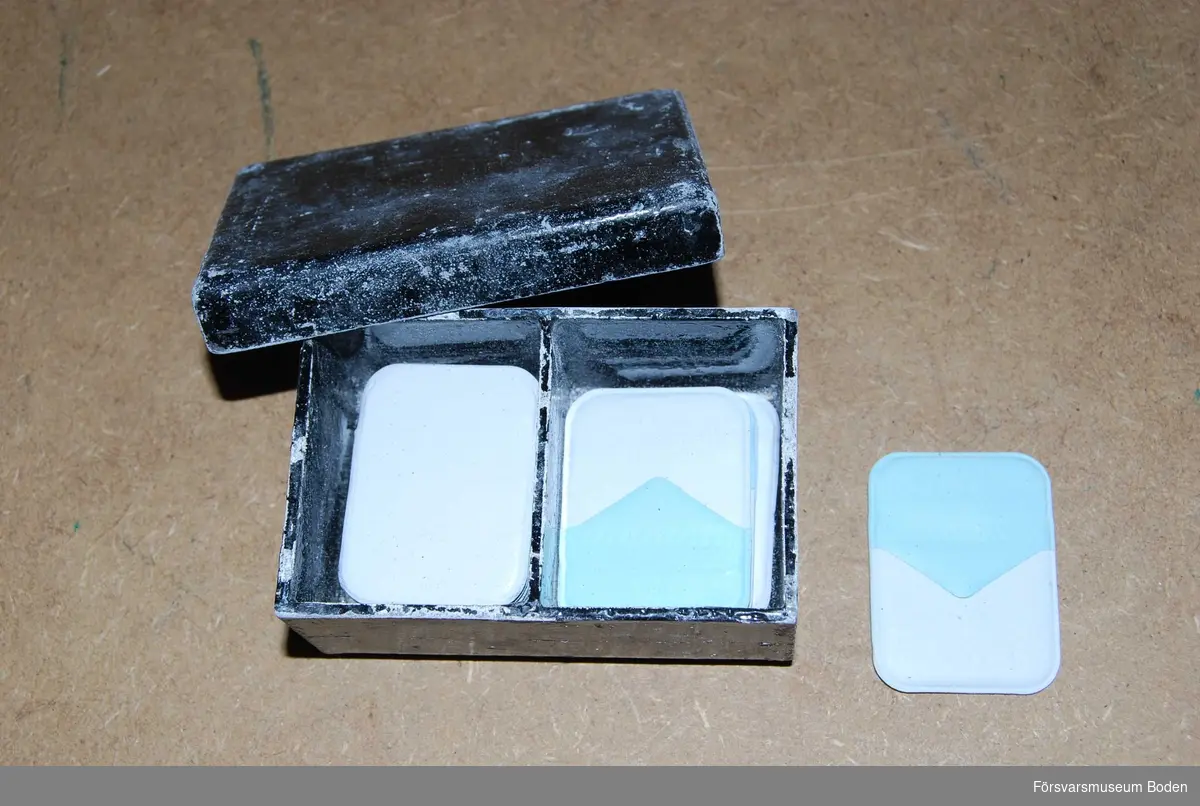Svartlackerad ask av bly indelad i två fack, innehållande ett antal oanvända Kodak röntgenplåtar för tänder.