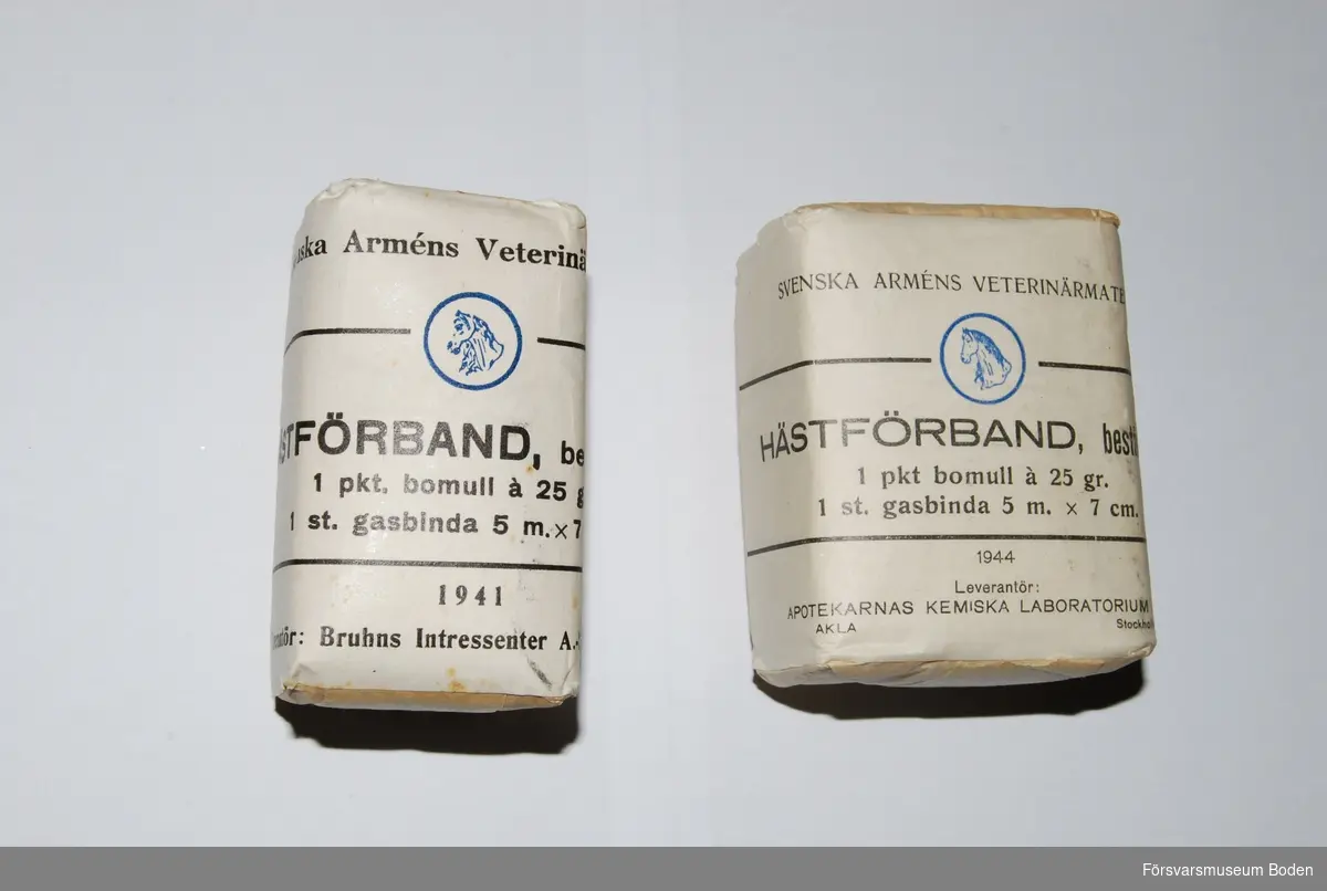 Två förpackningar från olika tillverkare, daterade 1941 respektive 1944. Varje förpackning innehåller ett paket bomull 25 g samt en gasbinda 5 m x 7 cm.