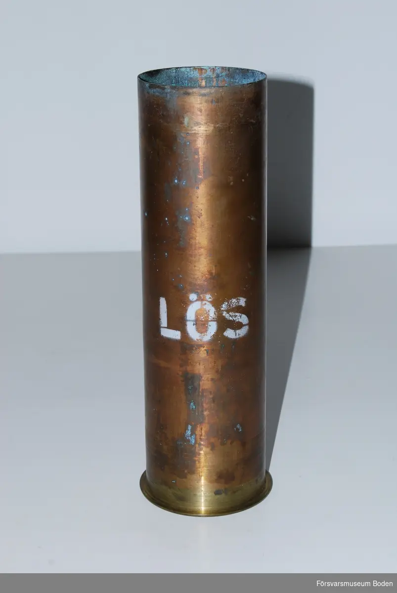 Patronhylsa från avfyrat salutskott. Av mässing med monterad tändskruv och texten "LÖS". Längd 278 mm.