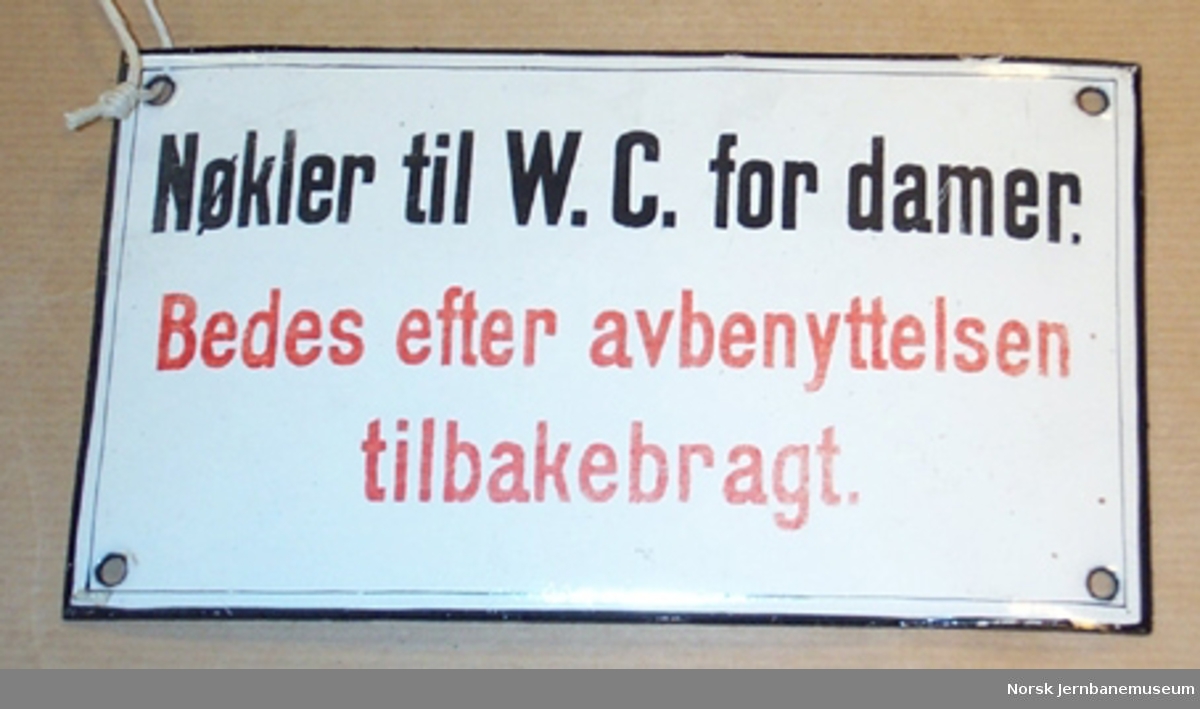 Skilt : "Nøkler til W.C. for damer. Bedes efter avbenyttelsen tilbakebragt." - fra jernbanestasjon