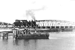 Smalsporet damplokomotiv foran et godstog på vei over Lågen 