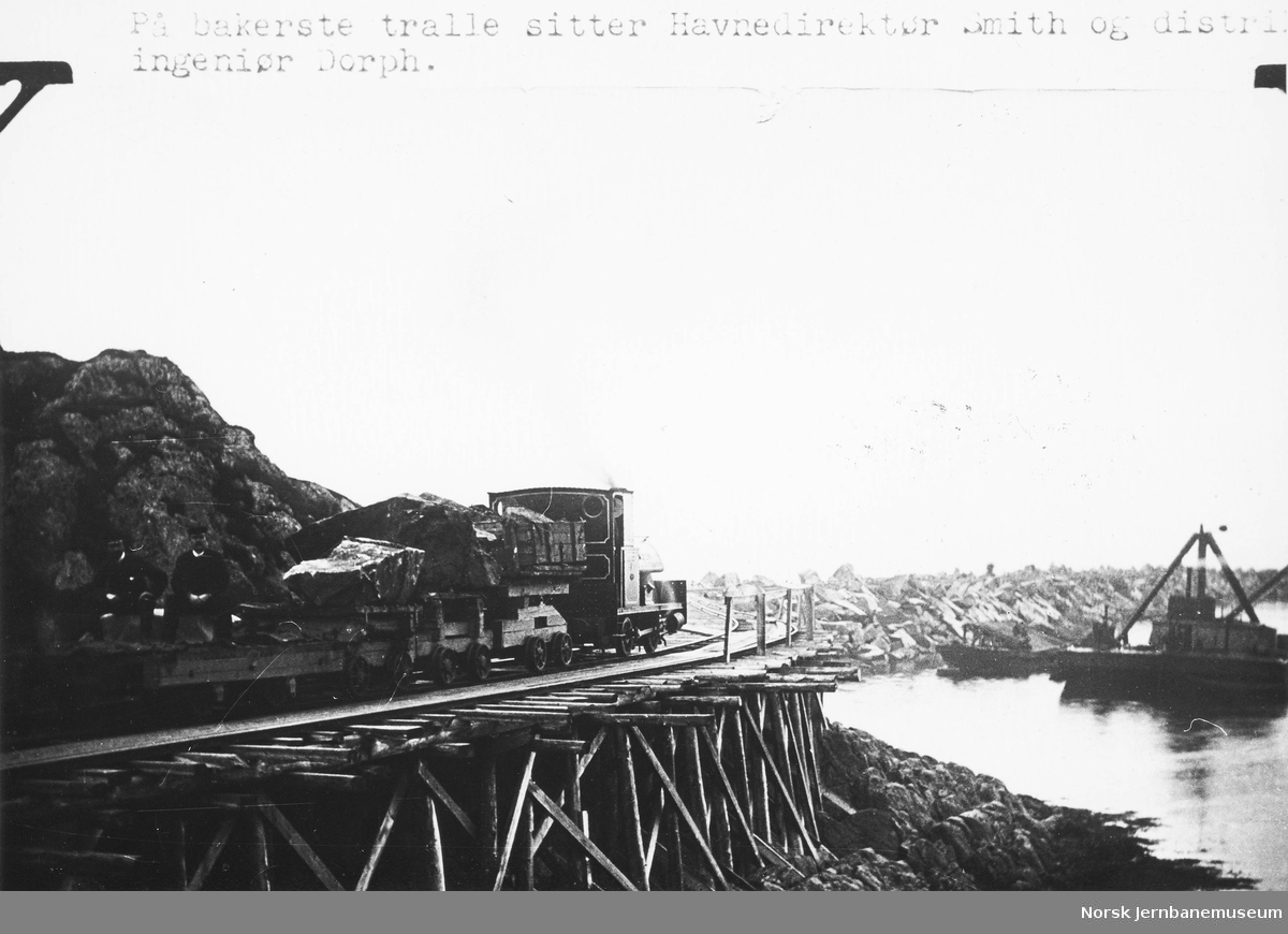 Statens Havnevesens damplokomotiv "Røiken" med steintraller på moloanlegget på Andenes; på bakerste tralle havnedirektør Smith og ingeniør Dorph