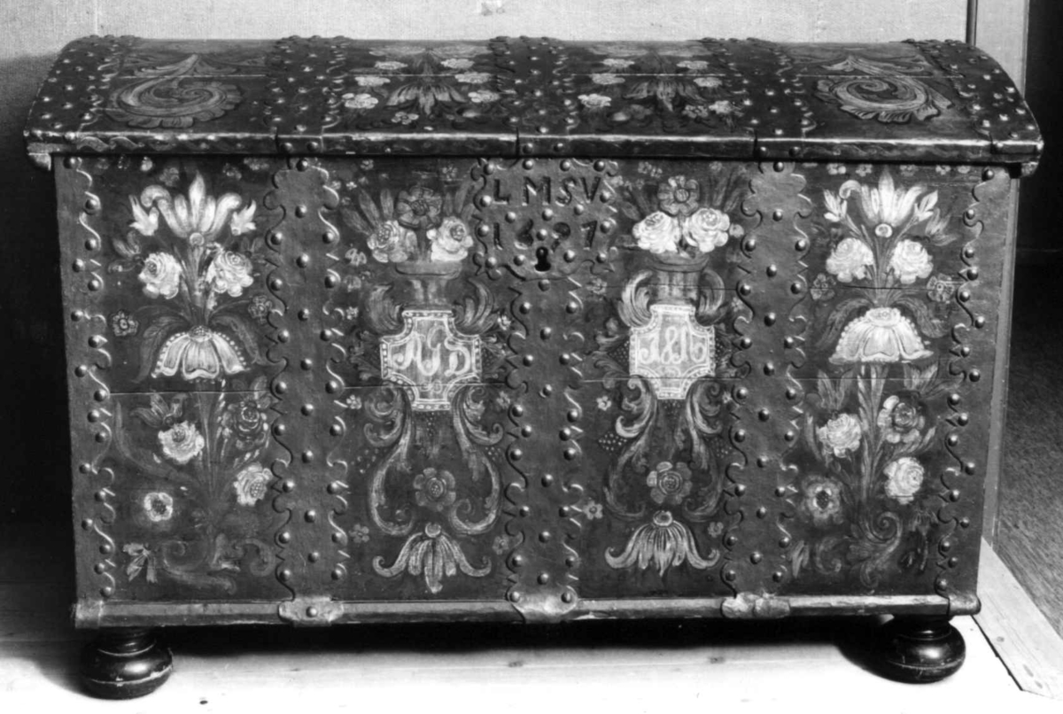 Kiste med buet lokk og heldekkende rosemaling, hvorav mye er senere tilføyelser eller restaureringer. Kulebena er også sekundære.