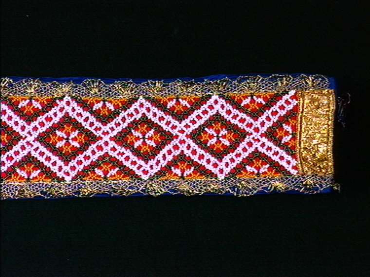 Flerfarget belte/korilistein med dekor av glassperler og metallbånd, kantet med blå silkebånd.