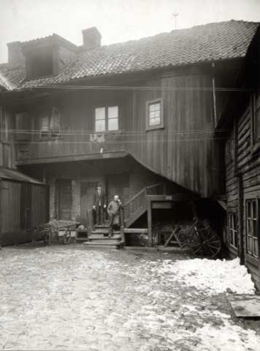 Hospitalgata 10, Oslo. Hjørnegård i tre med gårdsrom og uthus, to menn står i trapp.