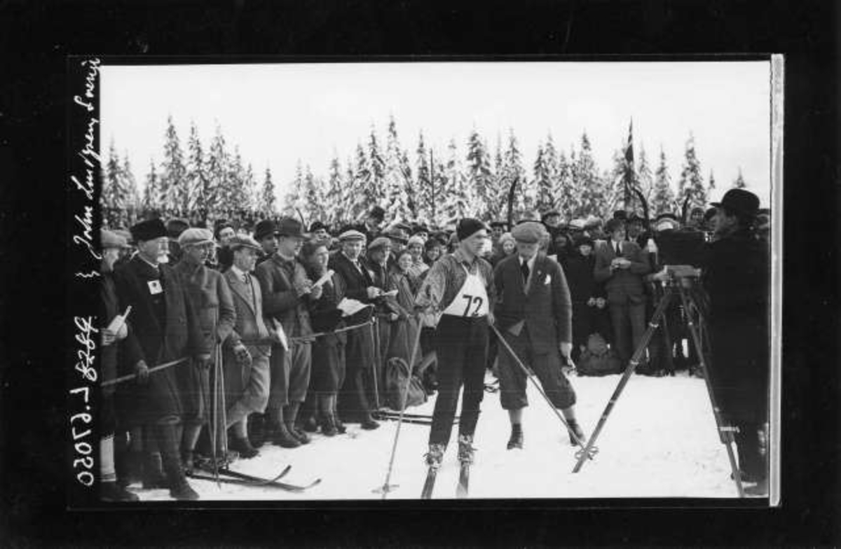 Vintermotiv. Ant. Nordmarka. Skirenn. Skiløper i sporet. Publikum langs løypa i skogen. Fotograf til høyre i bildet.