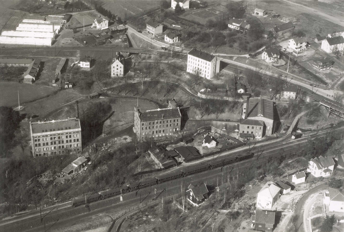 Bygninger ved A/S Joh. Petersens Linvarefabrik. Forstadsbane, jernbanespor og boliger. Gartneri i bakgrunnen.
