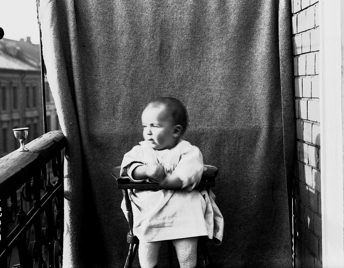 Lillebror Axel Q. Wiborg i barnestol fotografert på balkong, ant. Meltzers gate 9, Oslo, oktober 1899, mot opphengt bakteppe. 