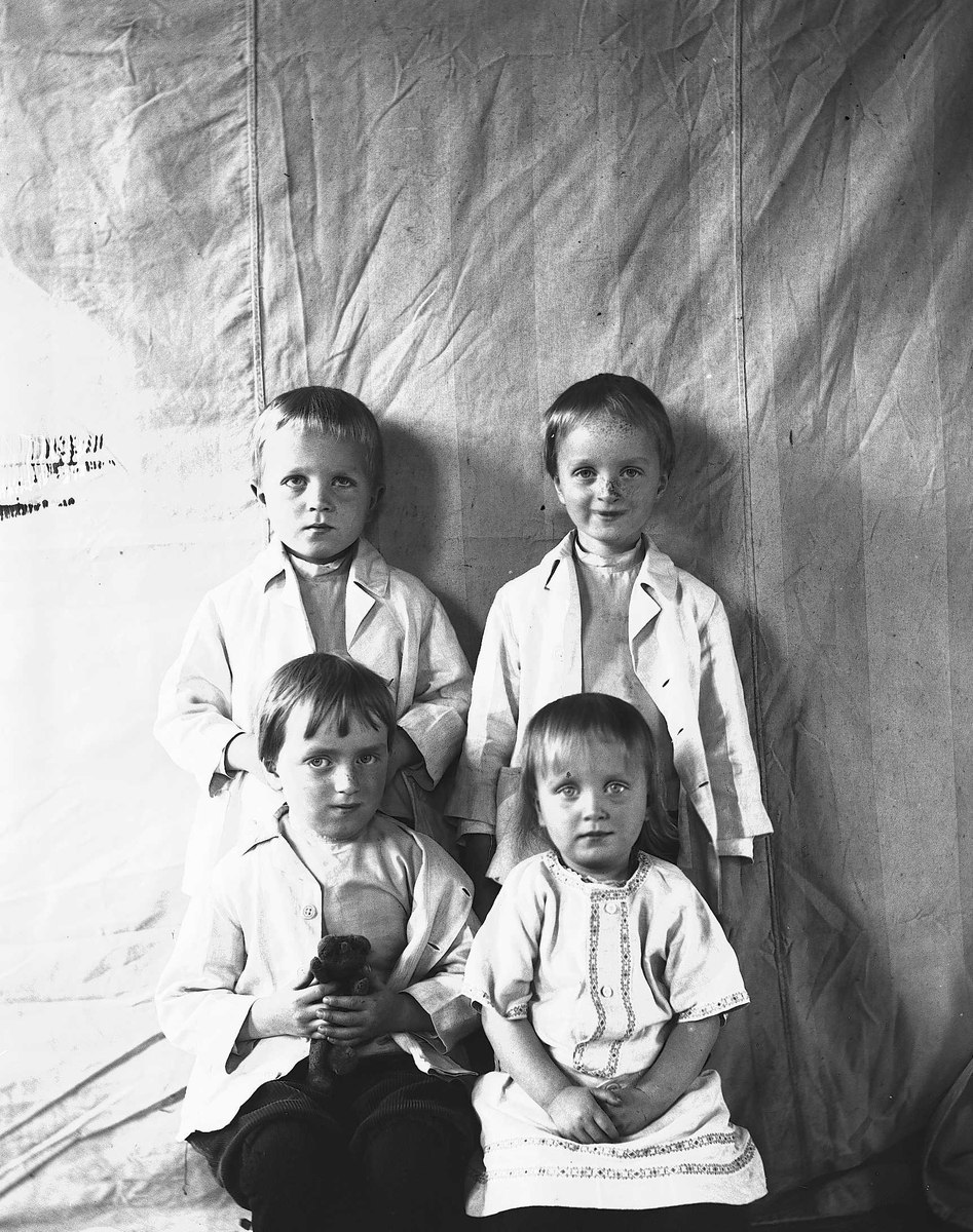 Portrett av fire barn, fotografert mot opphengt bakteppe, ukjent sted. Antatt er de barn i familen Axel Q. Wiborg.