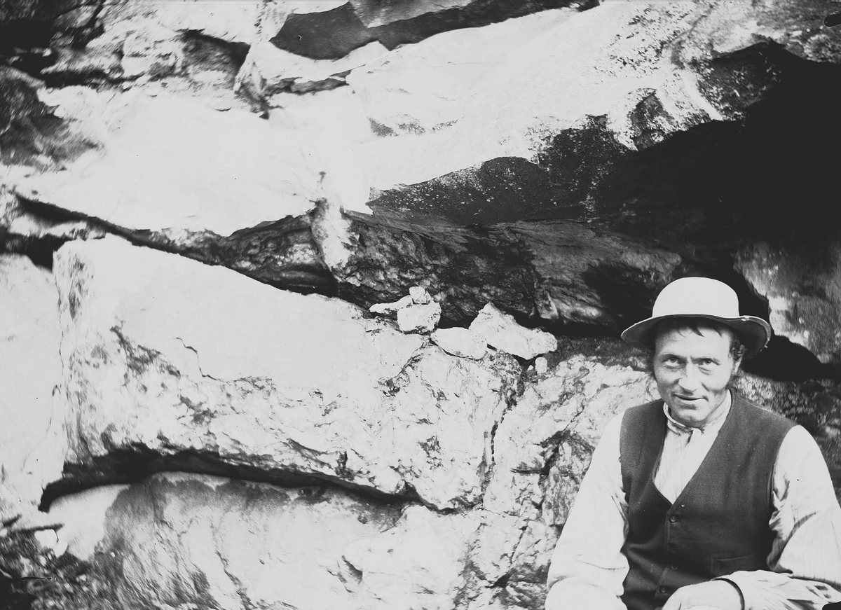 Nils B. Svensrud, fra Svensrud, Nore, Numedal, Nore og Uvdal, Buskerud, august 1906. Mann sitter foran bergvegg, ved kobbergruve.