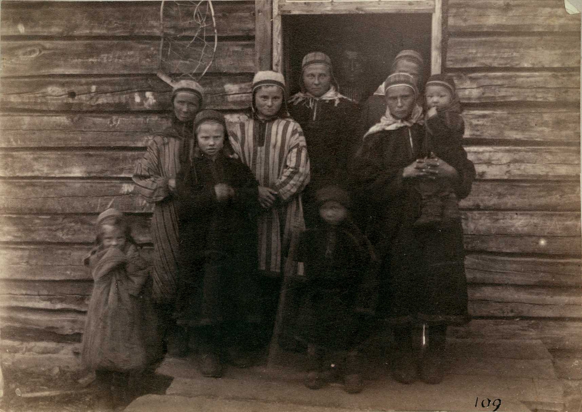 Norge. Kvinner og barn i samisk drakt, står foran døråpning.