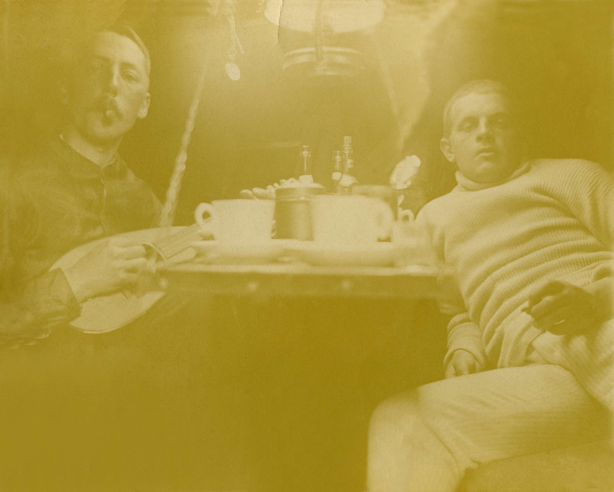 To menn ved et bord røyker sigar og spiller mandolin. Robsahm og Lund.