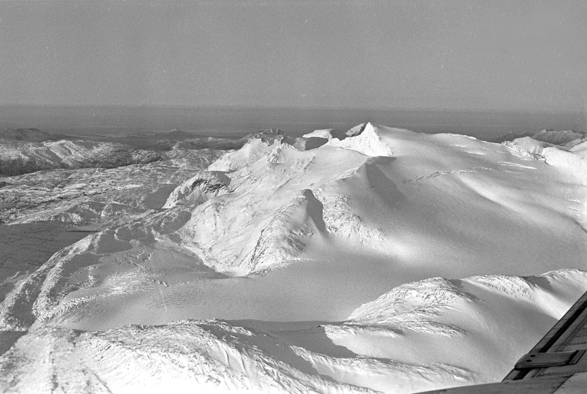 Serie. Ombord på SAS flyet til Tromsø. Flyfoto over snødekkete fjell. To flyvere i flytårnet. To menn og en kvinne, ant. Eva Lie, sitter rundt et bord. Fotografert desember 1965. 