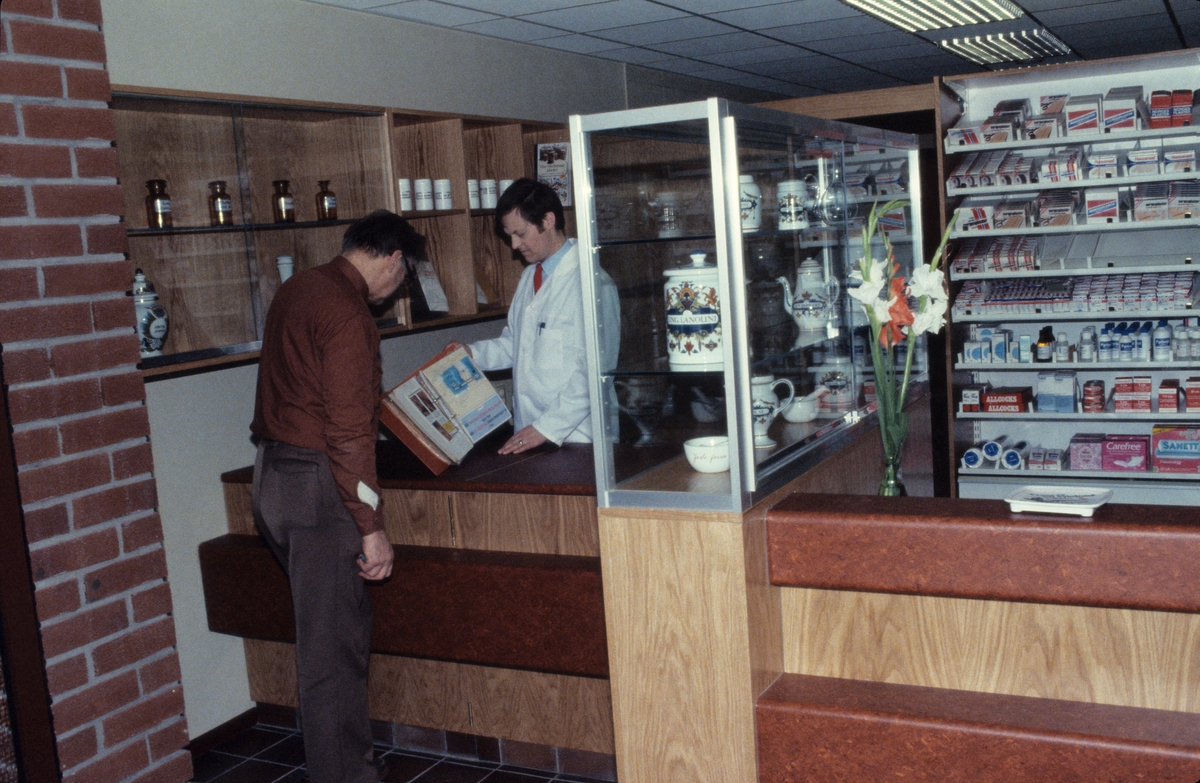 To menn ser i en perm ved skranken på Hemne apotek i Kyrksæterøra.