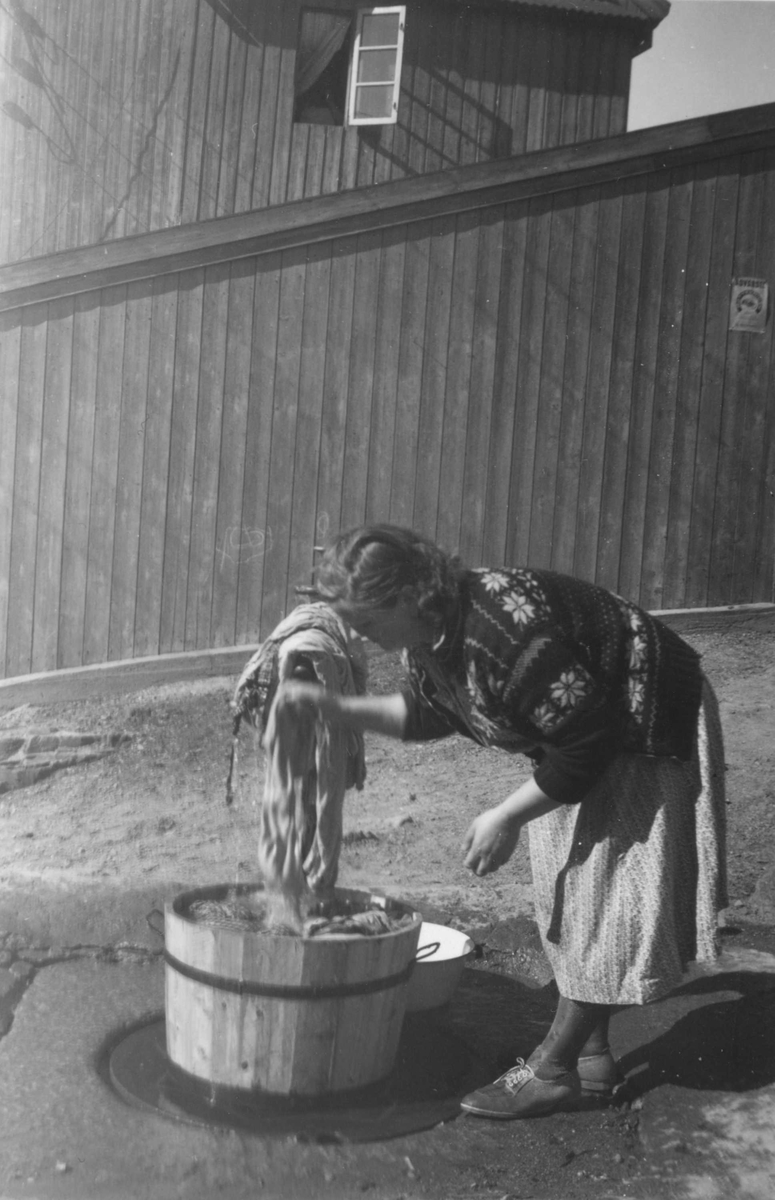 Fra trehusmiljøet på Enerhaugen, Oslo. Kvinne vasker tøy i lagget trestamp ved vannpost.