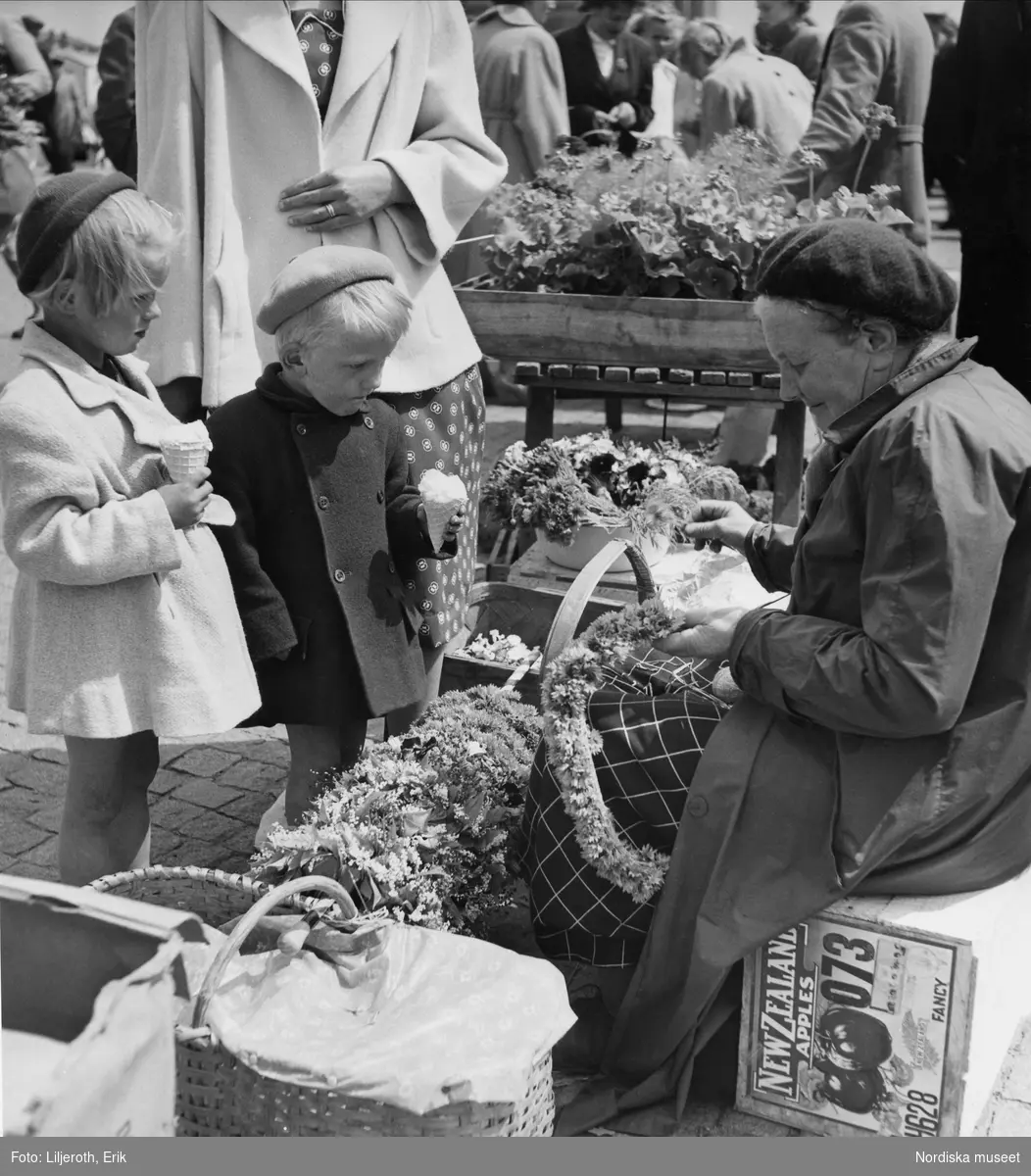 Två glassätande barn som tittar på en äldre kvinna som säljer blommor