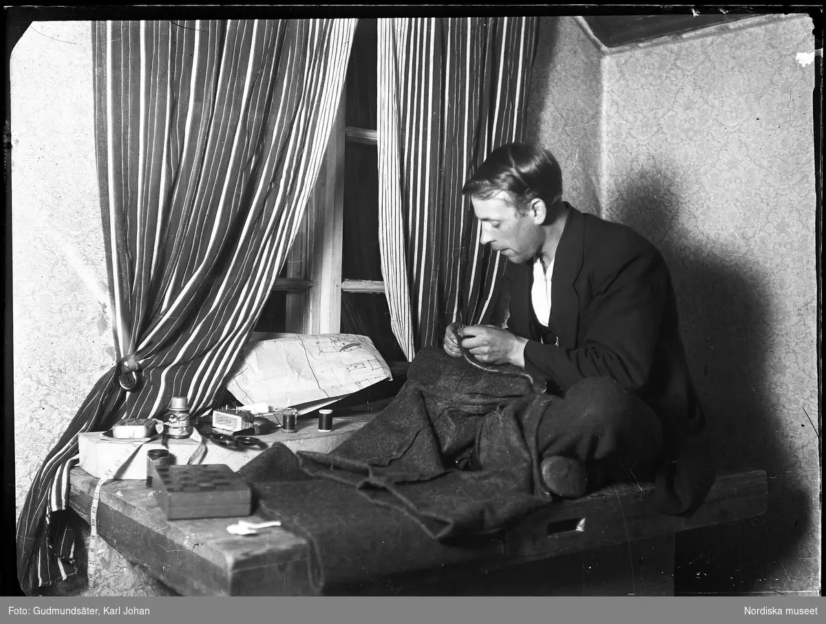 Skräddaren Ludvig Pihlström (1892-1967), sitter med korslagda ben på ett bord och syr.