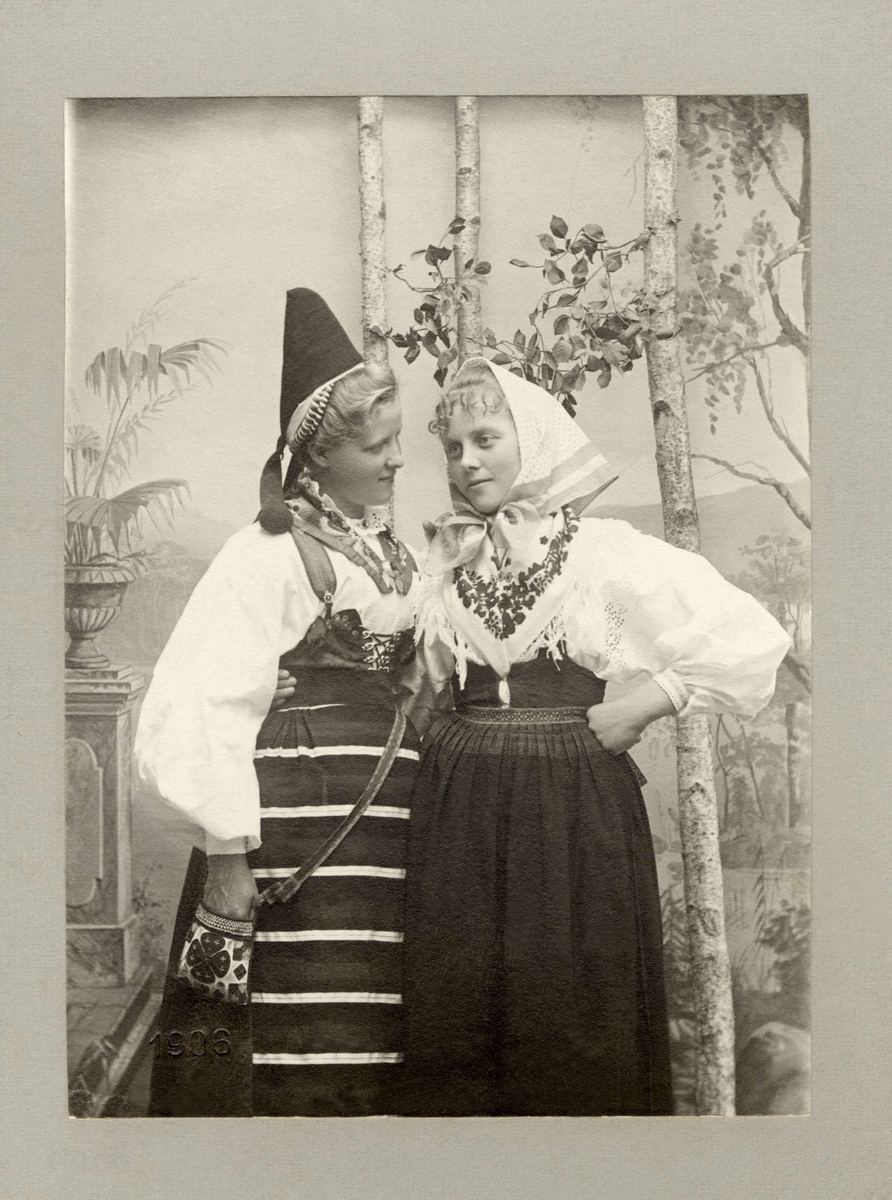 Två unga kvinnor poserar i olika folkdräkter