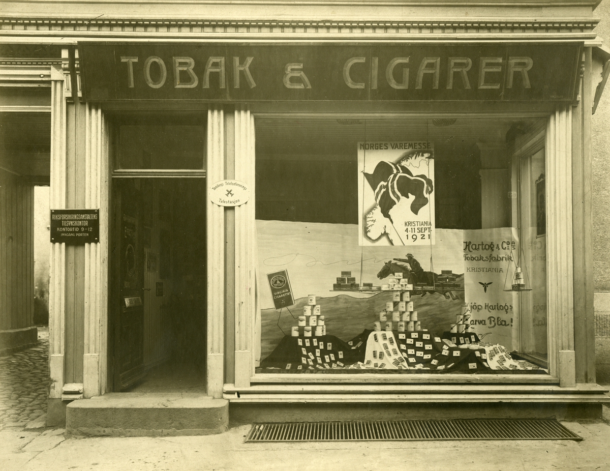 Vindusutstilling med reklame for bland annet Cromwell og Golden West sigaretter, Hartog Tobaksfabrik og Norges Varemesse i Oslo i 1921.