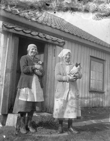 Enligt notering: "Två kvinnor, två katter, ett hus, systrarna Tyra o Klara Karlsson, Råröd ca 1922-23".