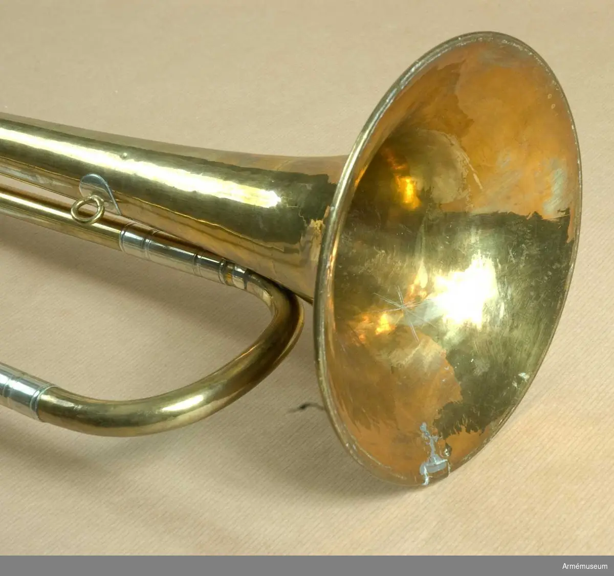 Höjd utan munstycke 69 cm, med d:o 72 cm. Av mässing och vitmetall med en vindling. Trumpeten är signerad på klockstycket Bohland & Fuchs, Graslitz - dock nästan bortputsat.