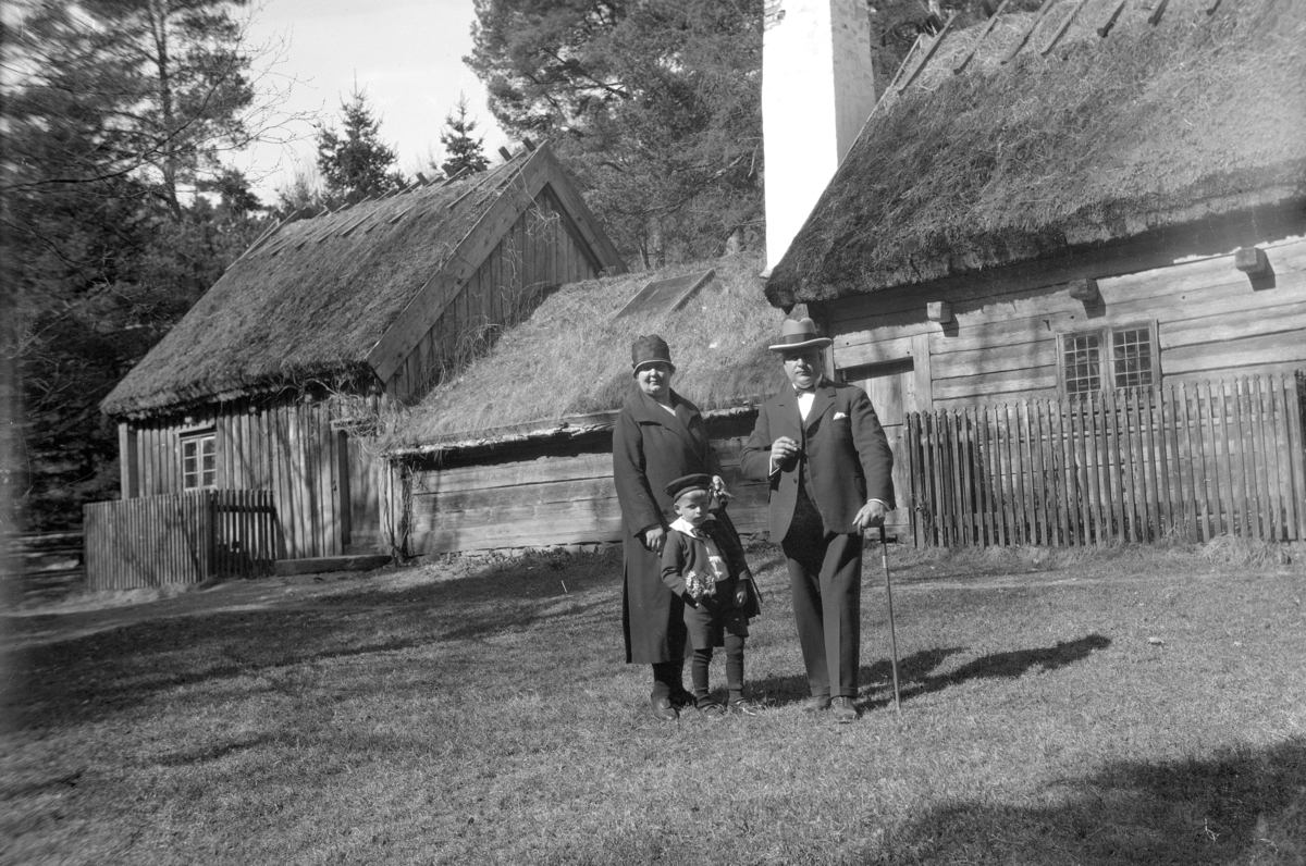 En familj framför Ryggåsstugan i Jönköpings Stadspark. Den är flyttad från Sjöaryds by, Markaryds socken, Sunnerbo härad.