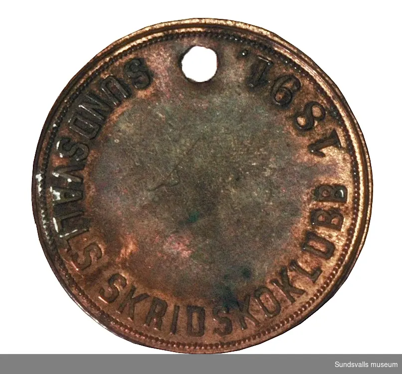 Medalj i koppar med text på aversen 'Sundsvalls Skridskoklubb 1891'. På reversen 'CC Sporrong & C0, Stockholm'.