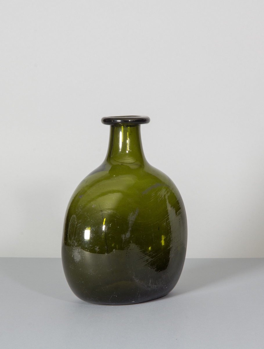 Flaska i grönt glas. Tillplattad modell med rundade sidor. Hals med bred halsring.
Likheter med den tyska Bocksbeutel.