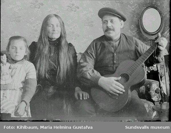 Familjeporträtt i rumsmiljö. Ester Näslund, Ljustorp, med föräldrar. Ester Näslund kom att arbeta som fotoassistent och senare fotograf i Maria Kihlbaums fotoateljé i Sundsvall.