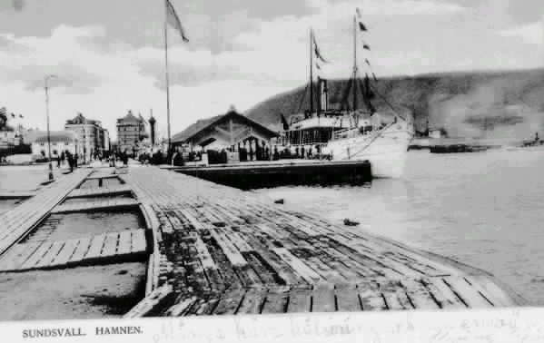 I bakgrunden en del av Tullpackhuset,  och magasinbyggnaderna kv Barkassen och kv Skonerten. Till höger passagerarbåten "J L Runeberg". Text på vykortet "Sundsvall. Hamnen".