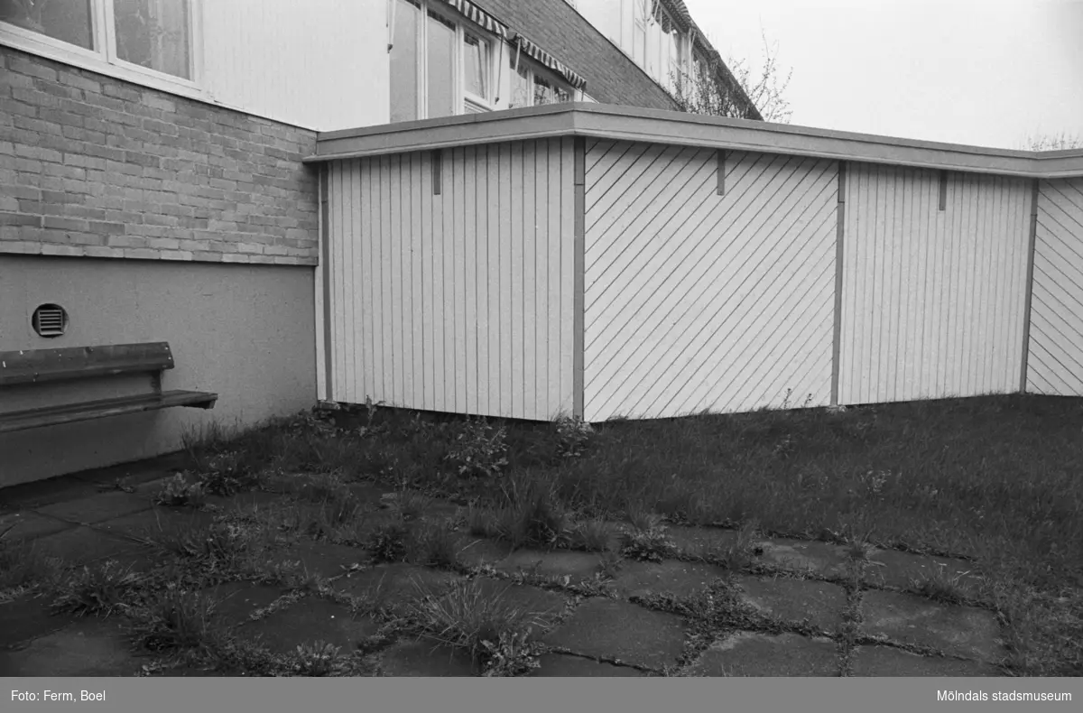 Dokumentation av Sagåsens flyktingförläggning 1992. Exteriör vy mot insynsskydd, bänk, gräsmatta och byggnad.