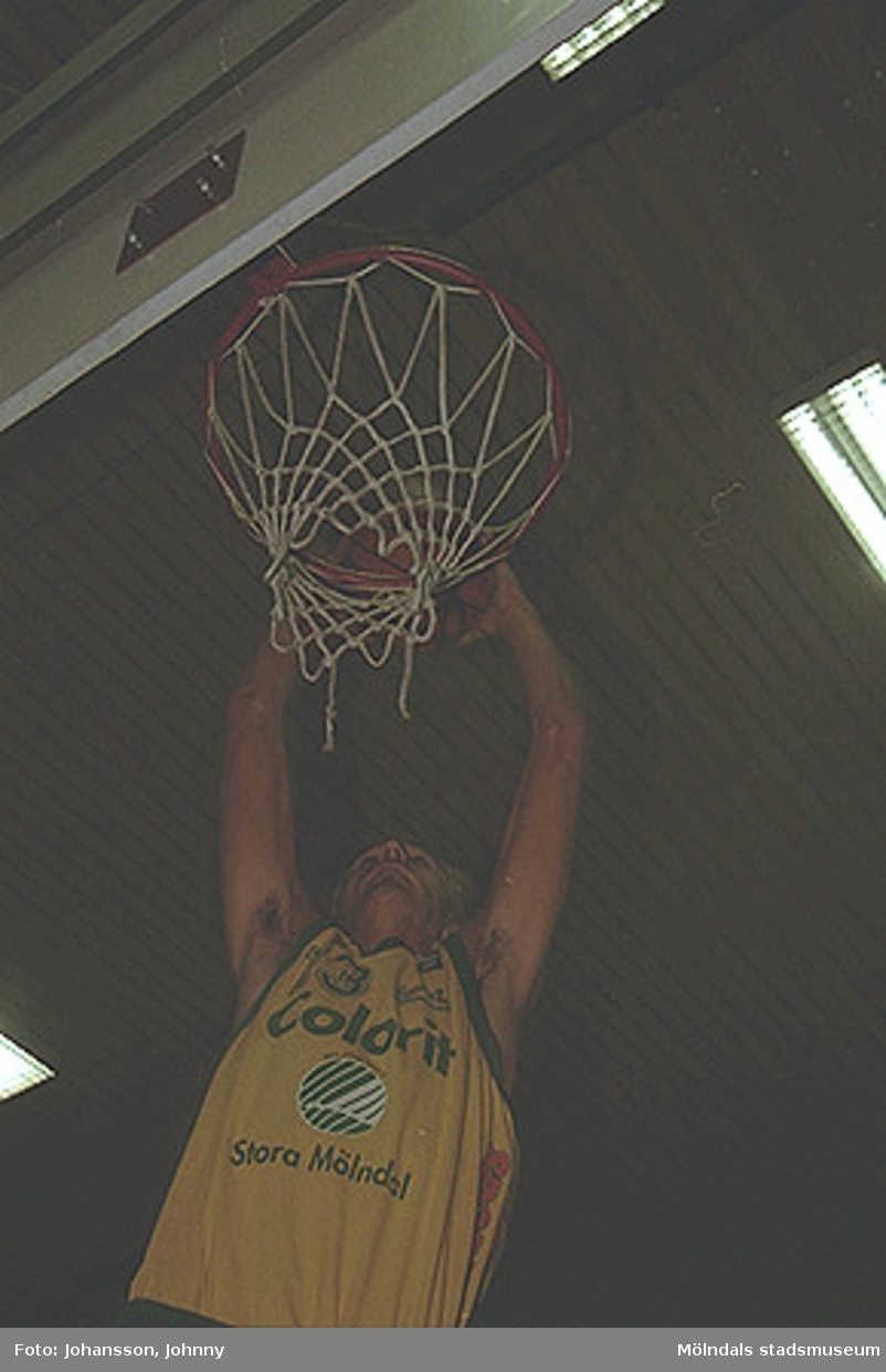 Basketspelare från Kvarnby basket som lägger mål. Han har reklamtryck Colorit på sin tröja. Kvarnby basket var på denna tid sponsrade av Stora Mölndal (f.d Papyrus).