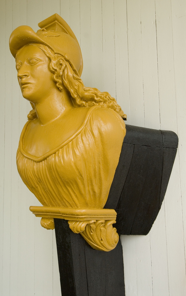 Galjonsbild tillhörande chefsfartyget Valkyrian.
Byst av hjälmprydd kvinna med långt lockigt hår liggande över ryggen, Bröstet täckt av klänning. Målningen blekt gulrosa och förstäven svart.