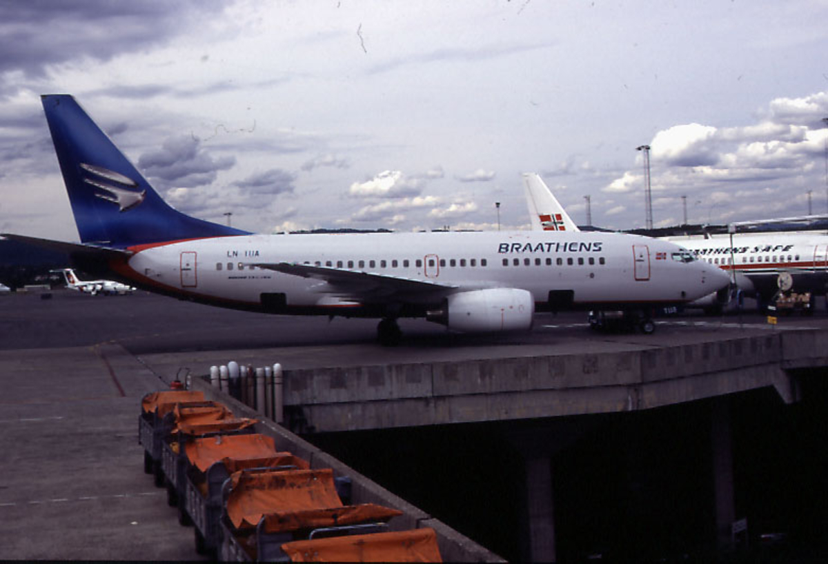 Lufthavn, 1 fly på bakken, Boeing 737-705, LN-TUA "Ingeborg Eriksdatter" fra Braathens.  5 baggasjevogner i forgrunnen, 2 andre fly i bakgrunnen.