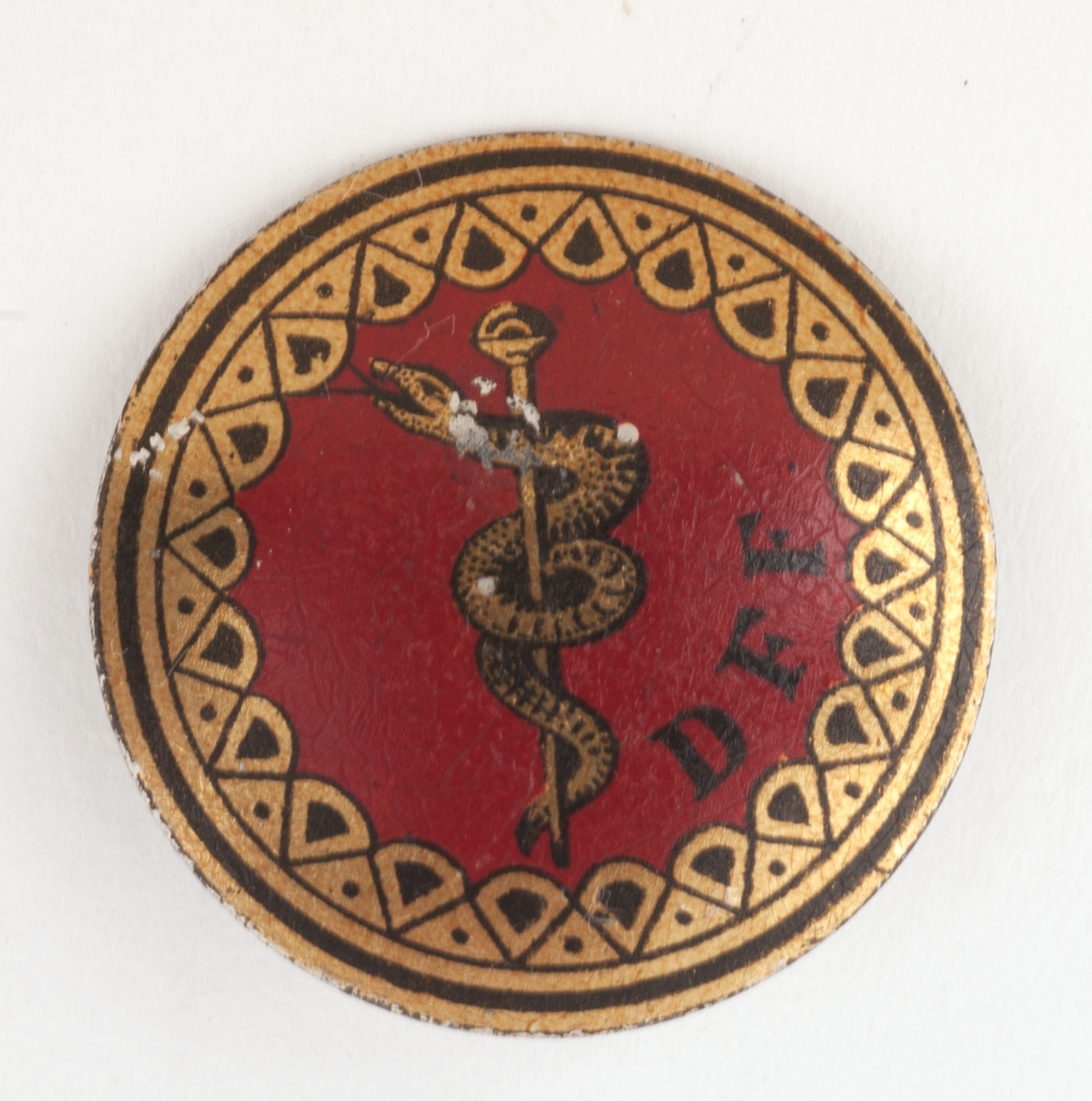 Rundt kongressmerke med logo (slange rundt en stav) festet til nål på baksiden