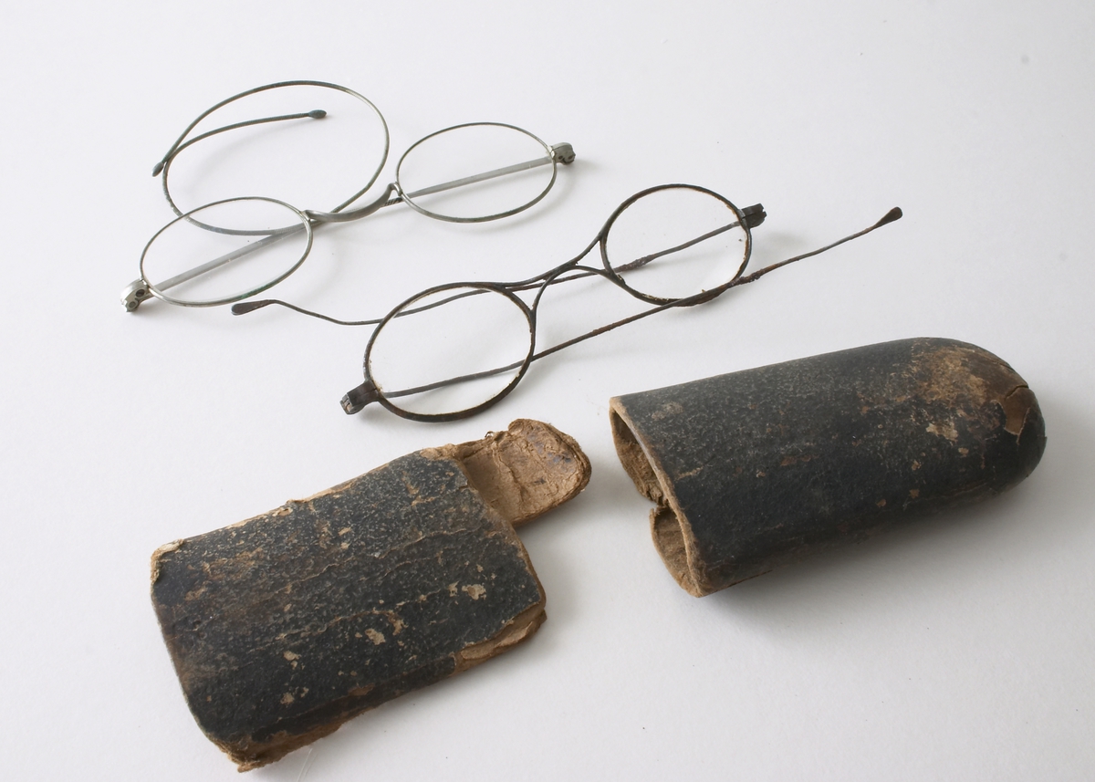 To par briller i et brillehus. Brillene er laget av metall og glass. Små ovale brilleglass, med innfatning. Det ene paret sannsynligvis av sølf - det andre av stål (med mye rust). Brillehuset består av to deler til å sette sammen laget av brun papp. Sølvbriller: L: med glass: 11,5 cm, L: Stang: 16,5 cm, Stål-briller: 11 cm; L: Stang: 12,5 cm, Brillehus L: 17 cm, B: 5 cm