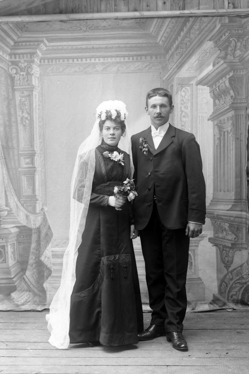 Studioportrett av et brudepar, med bruden i mørk kjole.