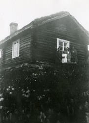 To kvinner og to jenter står foran en liten tømmerstue med t